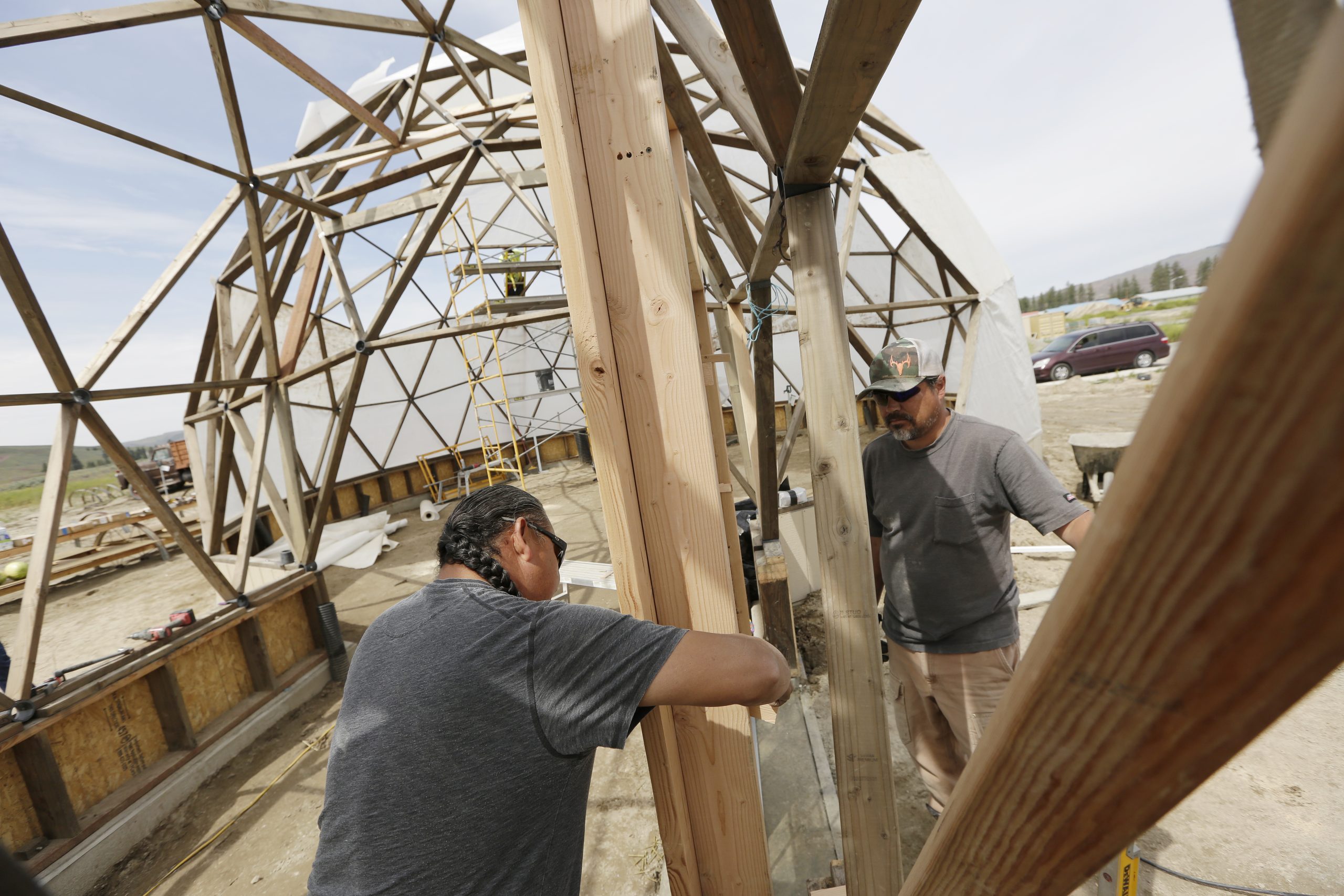 Ricky Gabriel, owner of Gabriel Construction and Development and strategic infrastructure partner with Konbit, left, and Doublas Lucht, trainee at Tribal Employment Rights Organization, install a door on a geodesic dome on Wednesday, June 15, 2022, in Nespelem, Washington.