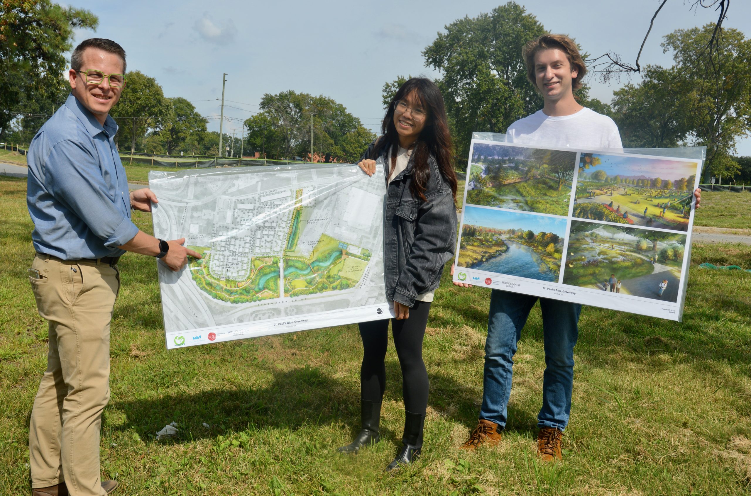 Three people stand in a field holding posterboard that depicts a landscape improvement project.