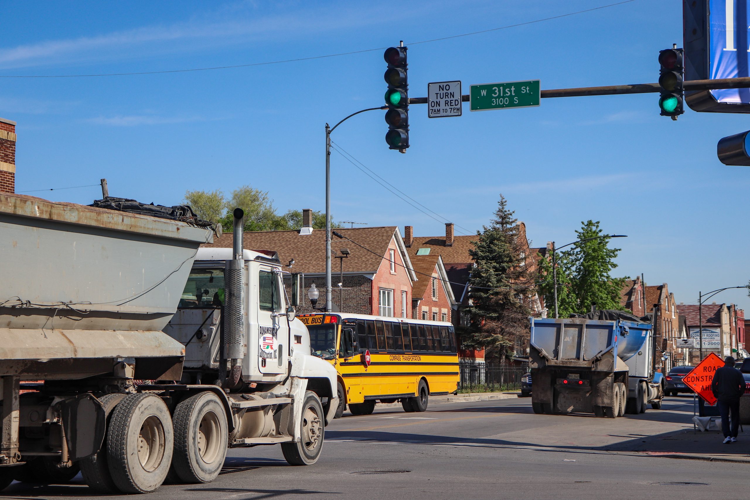 Two empty dump trucks drive northbound on Pulaski while a school bus drives south. A pedestrian can be seen walking south on Pulaski Rd. The 31st St. street sign is visible.